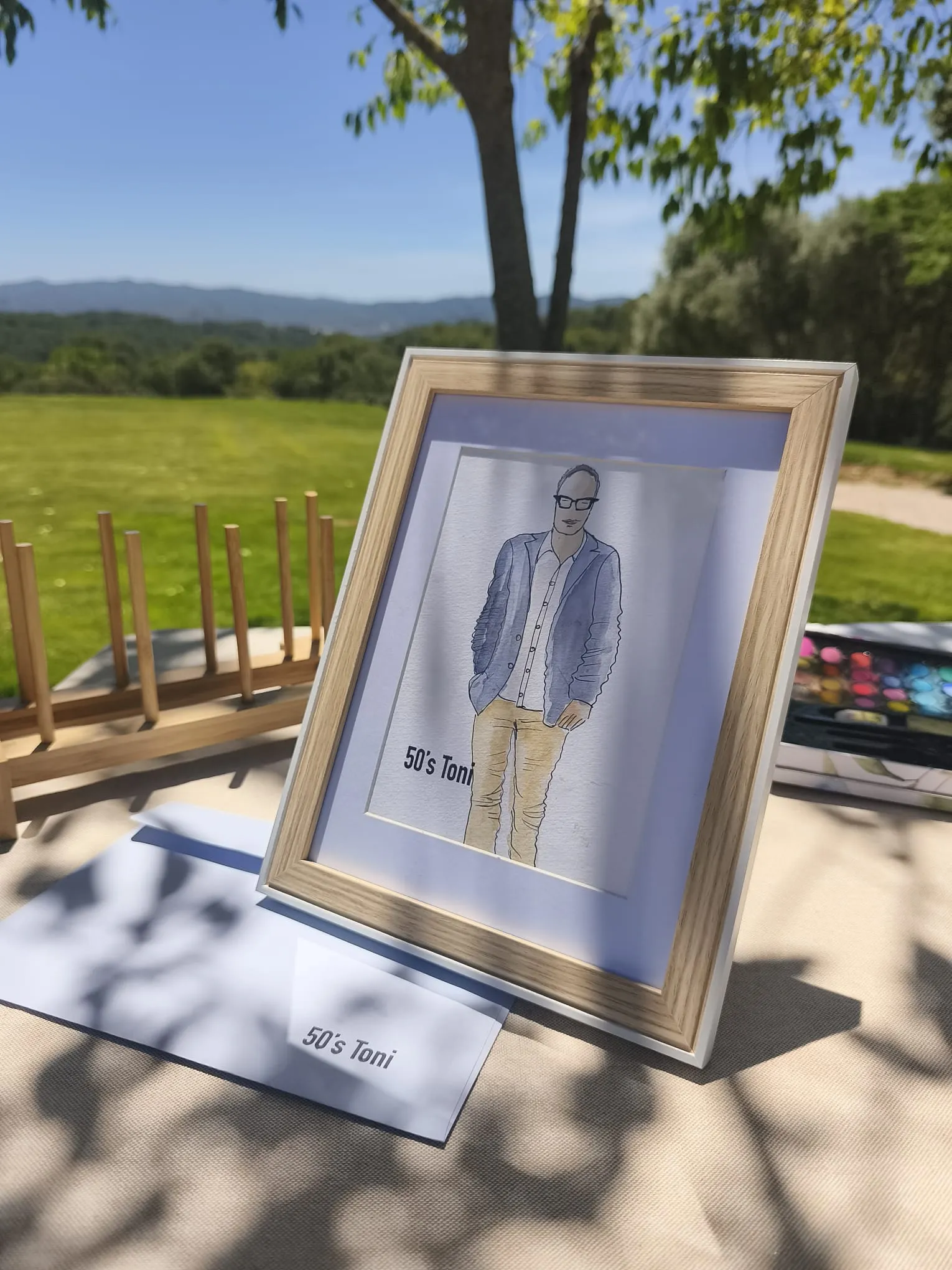 Il·lustració emmarcada sobre un cavallet amb el paisatge de camp al fons