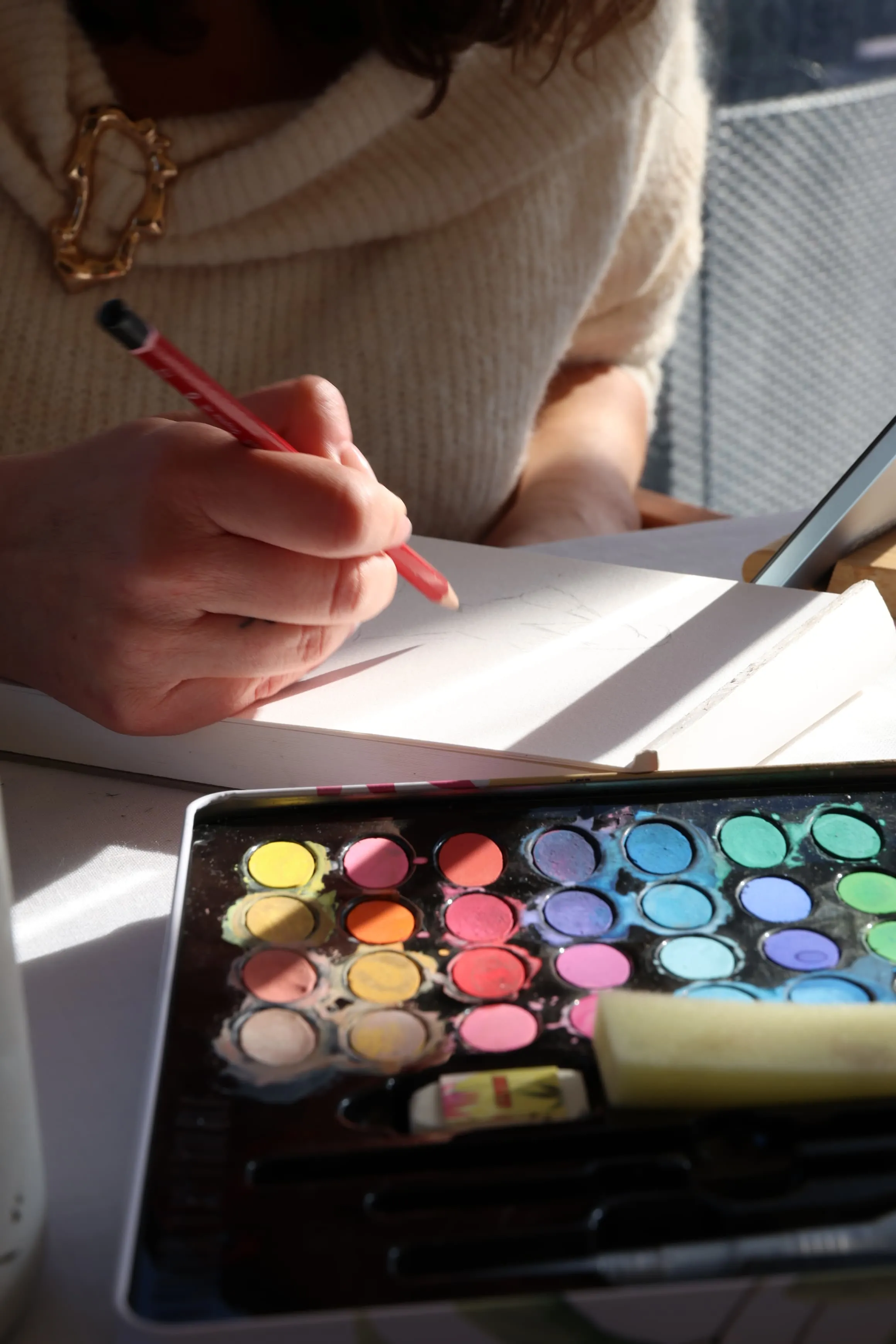 Mà traçant amb llapis vermell sobre paper amb la paleta d’aquarel·les al sol
